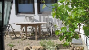A patio with a table and chairs, a stone wall, and a view of a building with windows and a door.