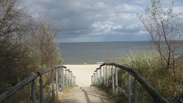 Ein hölzerner Weg führt zu einem Sandstrand, beidseitig gesäumt von einem Metallgeländer.