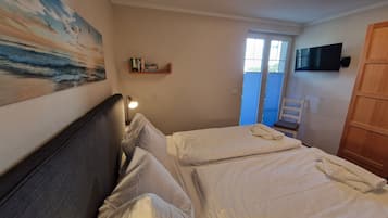 Ein Schlafzimmer mit zwei Betten, einem Nachttisch mit Lampe, einem Bücherregal, einem Fernseher und einem Fenster mit Jalousien.