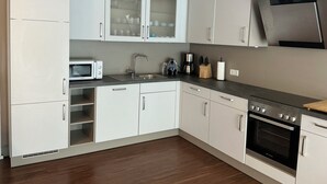 Een moderne keuken met witte kasten, een magnetron, een spoelbak, een koffiezetapparaat en een oven.