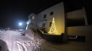 Een met sneeuw bedekte straat met een verlichte kerstboom voor een gebouw.