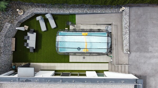 Una piscina sul tetto con un elemento d'acqua cristallina e blu, circondata da un muro in pietra e da una zona verde con posti a sedere all'aperto.