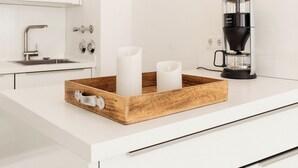 A modern kitchen with white cabinetry, a coffee maker, and a wooden tray with candles. - Modern comfort in Föhr's prime location (Nieblum)