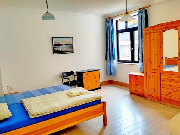 A bedroom with a bed, a wooden wardrobe, a desk, and a chair.