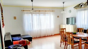 A living room with a sofa, a small table with a fan, a dining area with a table and chairs, and a TV on a cabinet. - 125m² Hohberg near Black Forest, Strasbourg, Europapark, Offenburg, Baden-Baden (Hohberg)