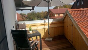 A wooden deck with a table and chair, a potted plant, and a white umbrella.