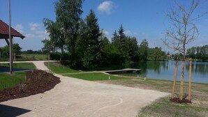 A gravel path leading to a dock over a lake, surrounded by trees and a building with a red roof.