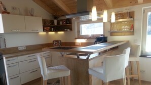 A modern kitchen with wooden cabinets, a central island with stools, and pendant lighting.