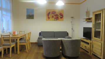 Un salon comprenant un canapé, deux fauteuils, un téléviseur, des meubles en bois et un tableau accroché au mur.