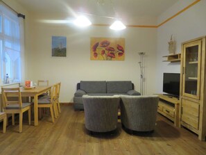A living room with a sofa, two armchairs, a TV, wooden furniture, and a painting on the wall. - Wittow - Pension Waldrose (Sellin)