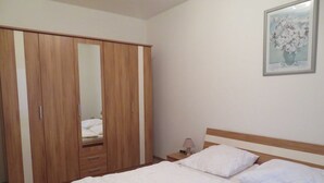 A bedroom with a wooden wardrobe, a bed with white bedding, a bedside table with a lamp, and a framed picture on the wall. - Wittow - Pension Waldrose (Sellin)