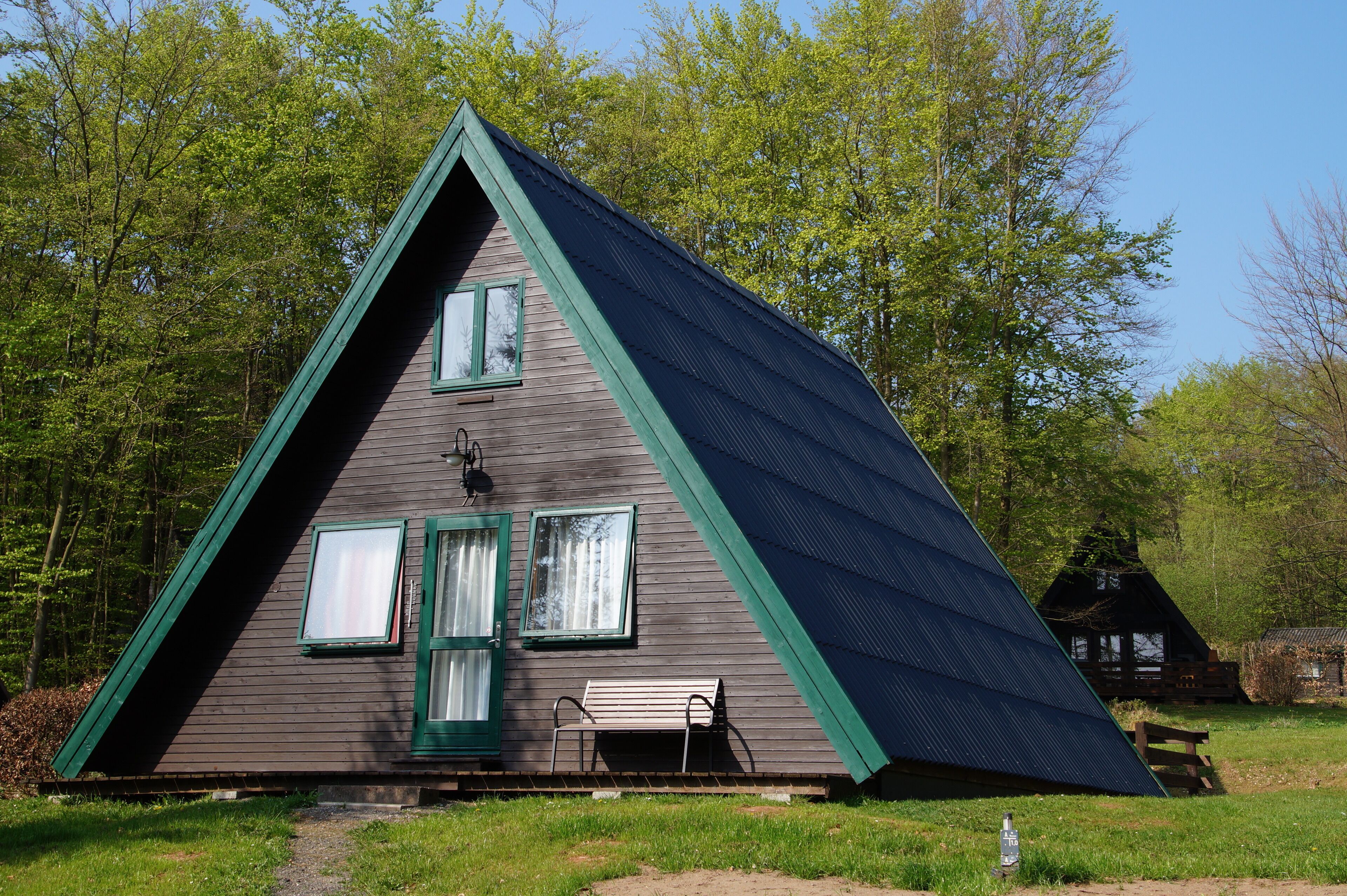 Una cabaña de madera triangular con dos ventanas y una banca afuera.
