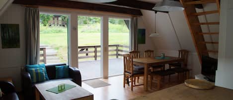 Una sala de estar acogedora con una mesa de madera, sofá y sillones, una mesa de comedor de madera y un ventanal con vistas a un jardín.