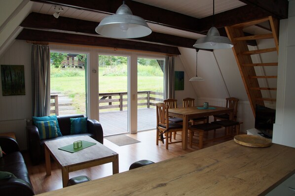 Una sala de estar acogedora con una mesa de madera, sofá y sillones, una mesa de comedor de madera y un ventanal con vistas a un jardín.