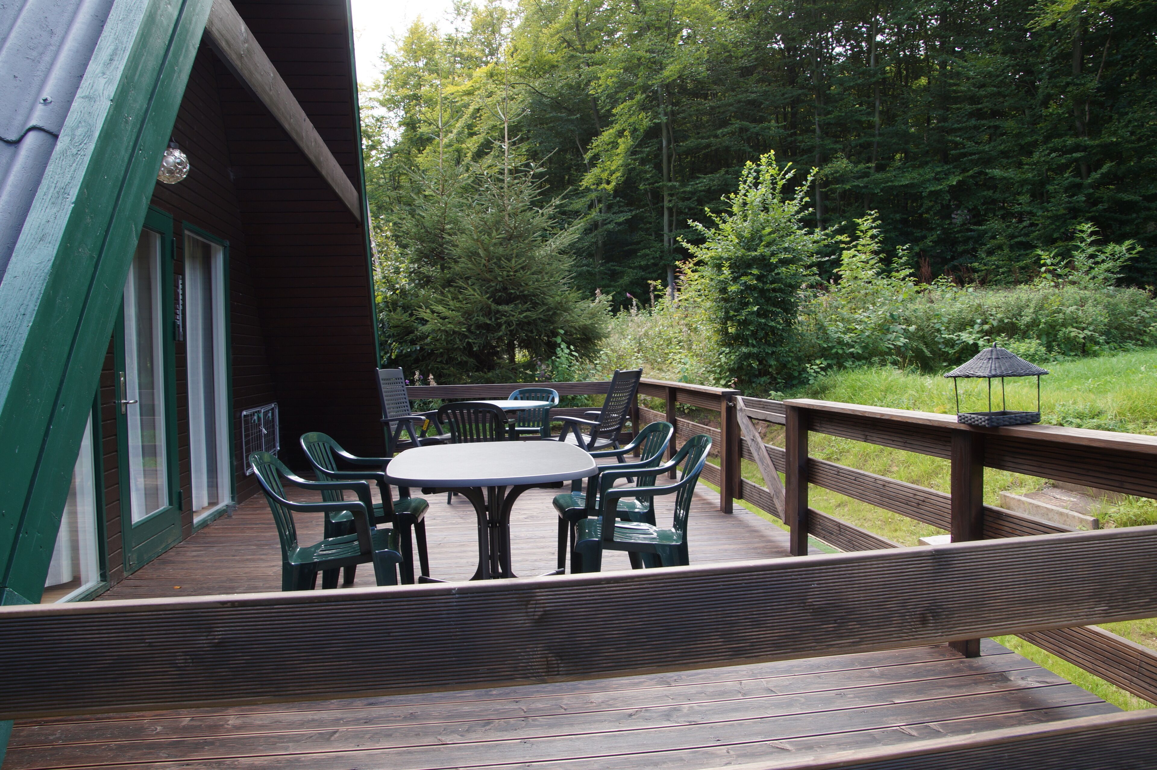 Een houten terras met een tafel en stoelen, omringd door begroeiing.