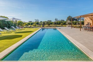 Ein rechteckiger Pool mit klarem Wasser, umgeben von einer gepflegten Rasenfläche und einer Terrassenanlage mit Gartenmöbeln.