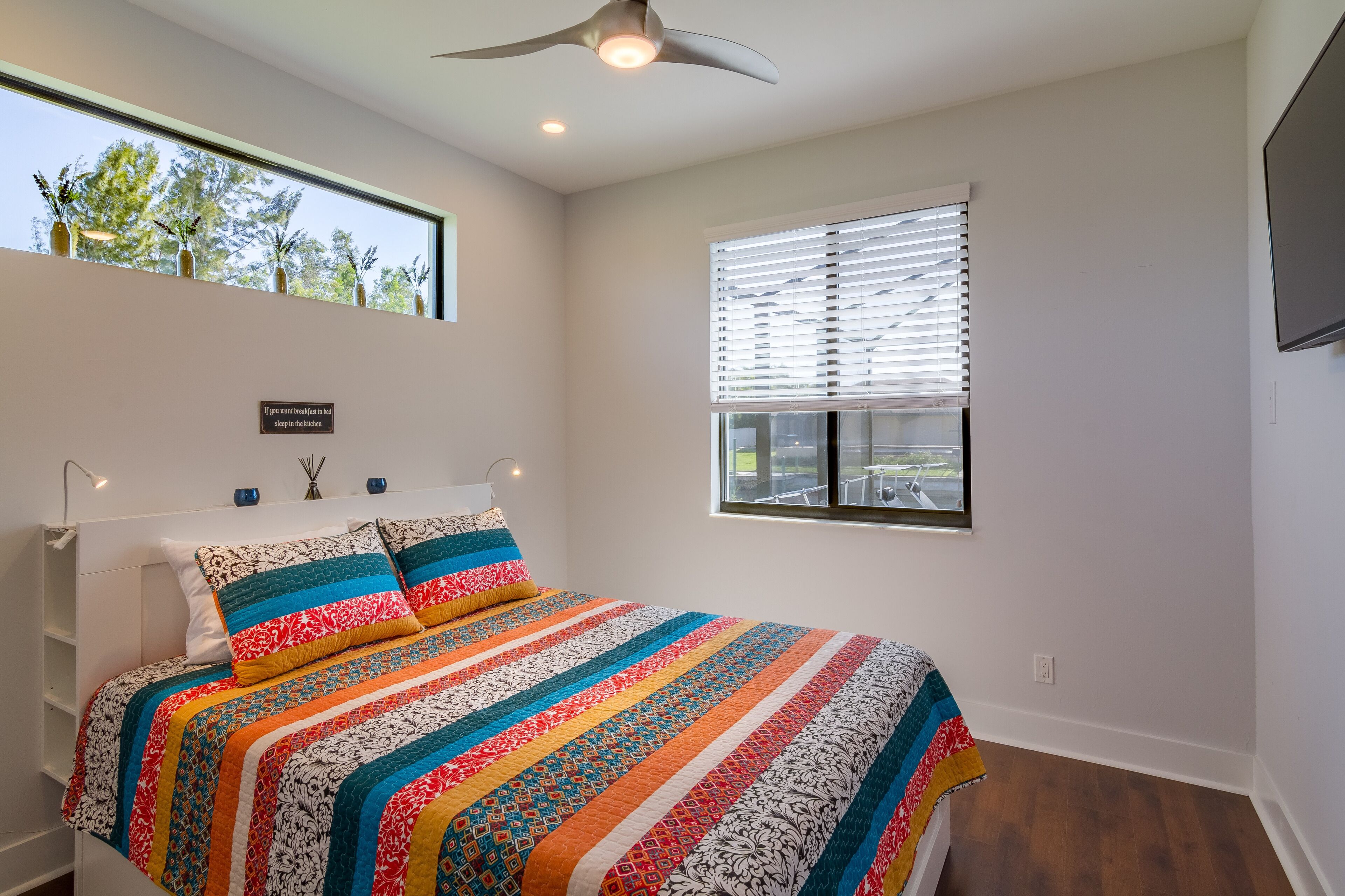 Un dormitorio con una cama grande, ventilador de techo, ventana con persianas y vistas al exterior.