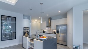 Une cuisine moderne dotée d’un îlot central, d’appareils électroménagers en acier inoxydable et d’une grande fenêtre.