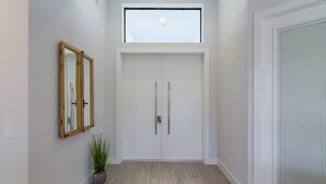 Un couloir avec une porte à deux battants, une petite fenêtre et une plante en pot.