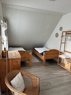 A small, cozy room with two wooden beds, a wicker chair, and a wooden dresser.