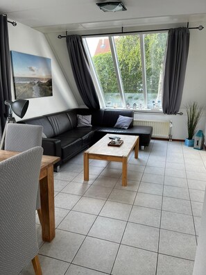 Relax in this stylish living room with a sofa, coffee table, and armchair, offering a view of lush greenery through the large window.
