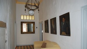 Un couloir doté d’un sol à carreaux, d’un canapé avec un coussin, d’un lustre et de portraits encadrés accrochés au mur.