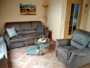 A living room with a brown leather sofa, a glass coffee table, and a gray armchair. - Non smoking apartment, ideal for 2 to 4 persons, quiet place suitable for allergy sufferers, (Stedesdorf)