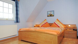 A bedroom with a wooden bed, a nightstand, a lamp, a window with curtains, and a painting on the wall. - Non smoking apartment, ideal for 2 to 4 persons, quiet place suitable for allergy sufferers, (Stedesdorf)