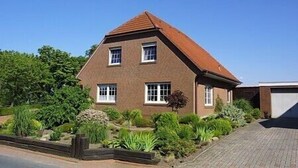 A two-story brick house with a sloped roof, surrounded by a garden with various plants and shrubs. - Non smoking apartment, ideal for 2 to 4 persons, quiet place suitable for allergy sufferers, (Stedesdorf)