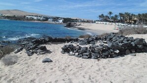 En strand med klippformationer i förgrunden, en sandstrand och en kuststad i bakgrunden.
