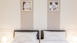 Une chambre d’hôtel avec deux lits, chacun doté d’un oreiller blanc et d’une tête de lit. Deux lampes murales sont fixées de chaque côté des lits.