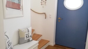 Una habitación con una puerta azul, un banco blanco con cajones y un cuadro colgado en la pared.
