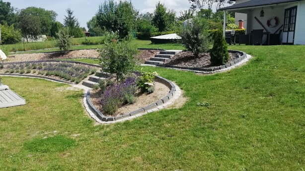 Un jardín ajardinado con una terraza de madera, un pérgola y diversas plantas.