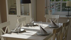 Una mesa de comedor con sillas blancas, una lámpara colgante negra y una ventana con vistas a zonas verdes.