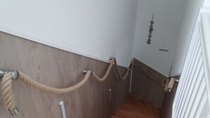 Una escalera de madera con barandilla de cuerda, paredes blancas y suelo de madera.