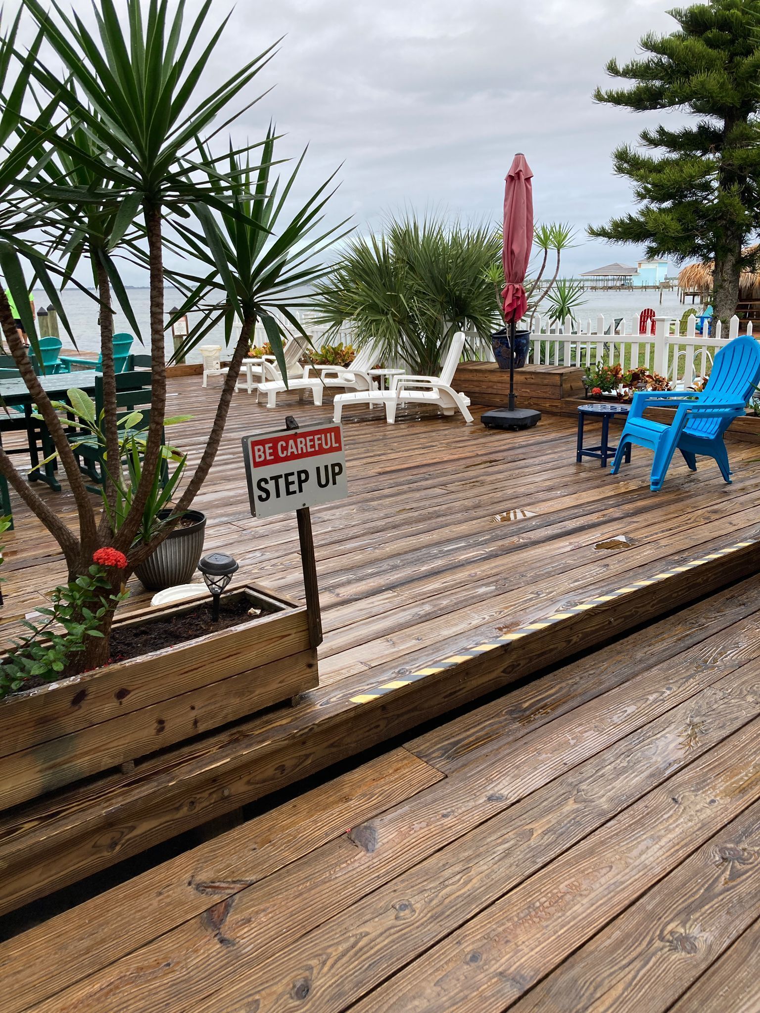 Un ponte in legno con poltrone da relax, un cartello che riporta la scritta “BE CAREFUL STEP UP” e vista sull'oceano.