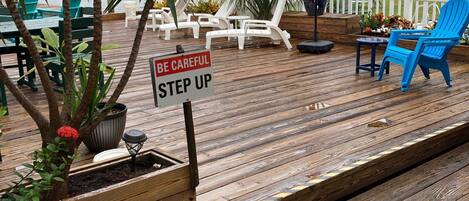 Un ponte in legno con poltrone da relax, un cartello che riporta la scritta “BE CAREFUL STEP UP” e vista sull'oceano.