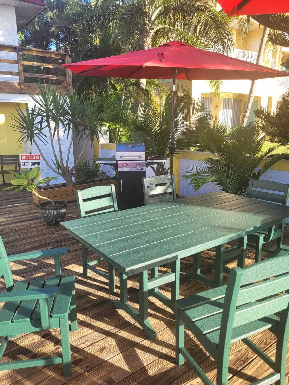 An outdoor patio with a green table and chairs, a red umbrella, and a barbecue grill.