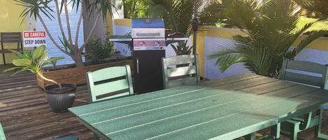 An outdoor patio with a green table and chairs, a red umbrella, and a barbecue grill.