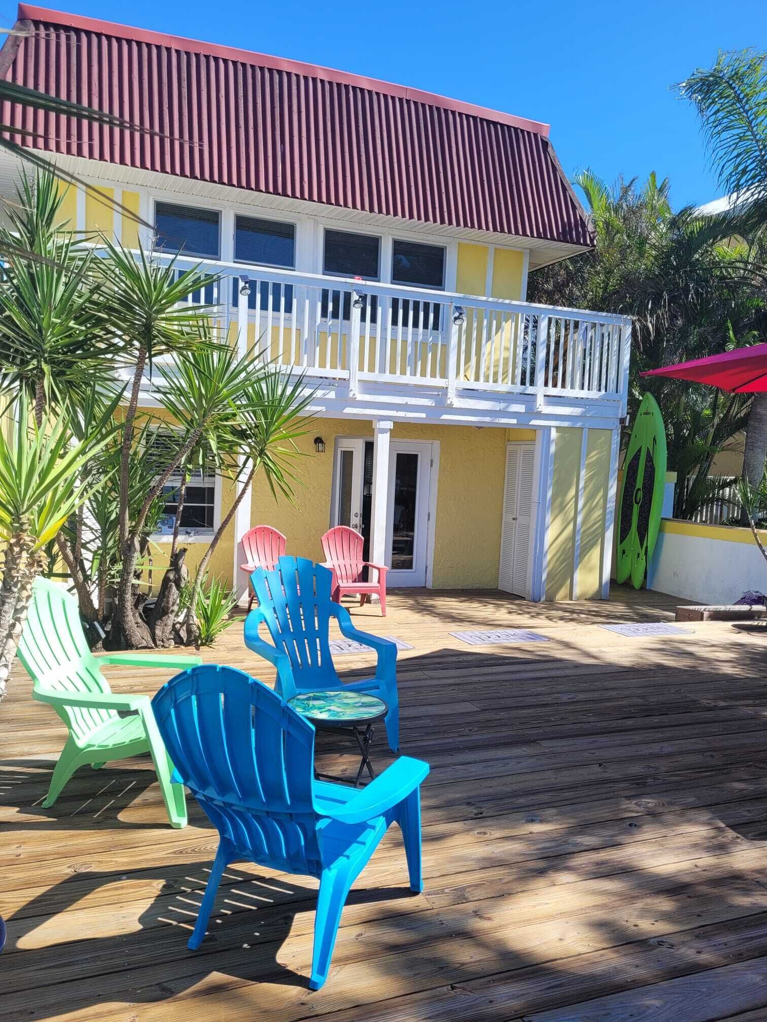 A two-story building with a balcony, outdoor seating with chairs, and a wooden deck.