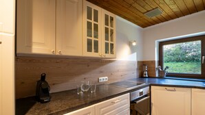 Uma cozinha com armários brancos, teto de madeira e janela com vista para um jardim.