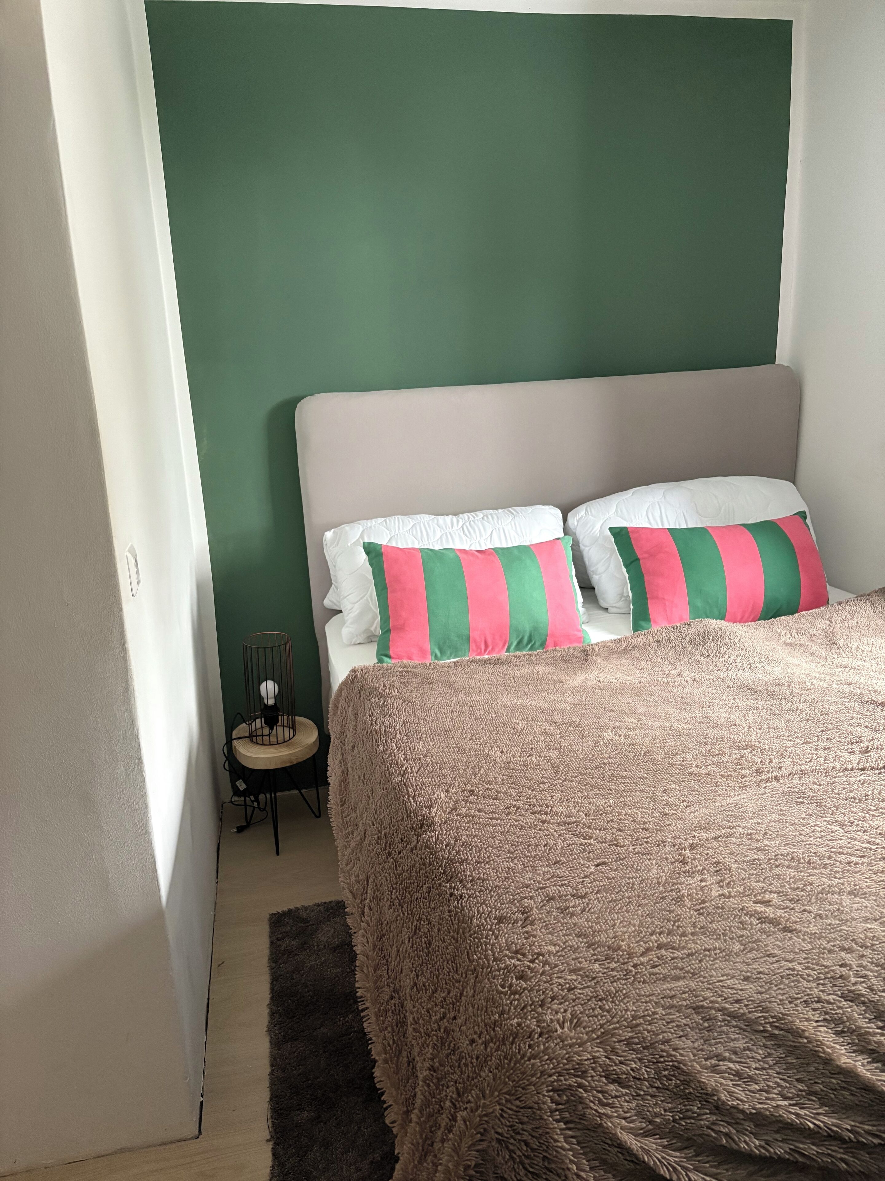 A bedroom with a green wall, a beige headboard, and a brown textured bedspread.