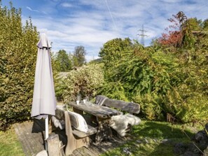 Eine Holzbank und ein Sonnenschirm in einem Garten mit üppigem Grün und blauem Himmel.