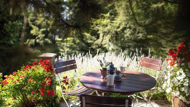 An outdoor dining area with a round table and chairs, surrounded by lush greenery and flowering plants. - Best starting point for bikers, hikers, mushroom and nature lovers in the national park  (Bohinj -Koprivnik)