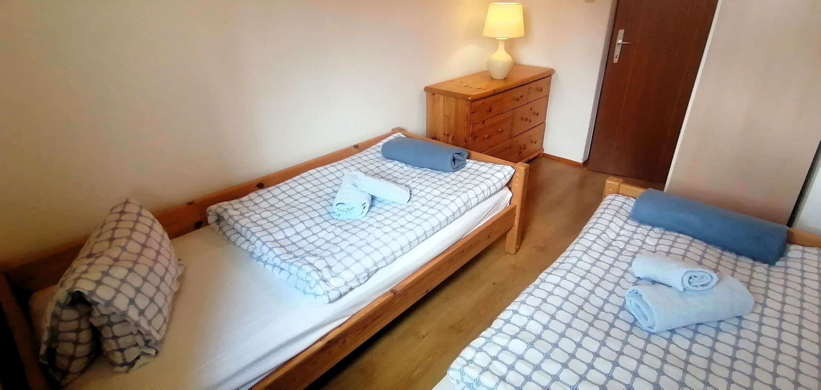Zwei Einzelbetten mit gemusterten Bettdecken, ein Nachttisch aus Holz mit Lampe sowie ein Holzschrank.