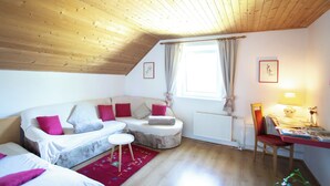 A cozy room with a wooden ceiling, a white sofa with red cushions, a small round table, a radiator, and a window with curtains. - Best starting point for bikers, hikers, mushroom and nature lovers in the national park  (Bohinj -Koprivnik)