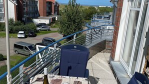 Un balcon avec une table dressée pour deux personnes, une bouteille de vin et une vue sur la mer et les bâtiments.