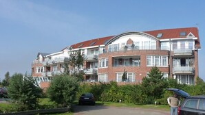 Un immeuble résidentiel à plusieurs étages, doté de balcons, d’un toit incurvé et d’une façade en briques.