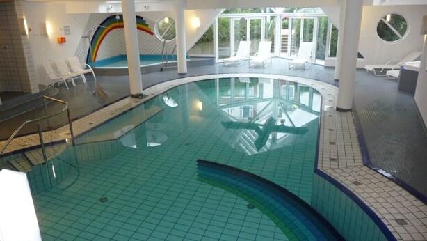 Une piscine intérieure au design incurvé, entourée de chaises longues blanches et agrémentée d’une fresque aux couleurs de l’arc-en-ciel.
