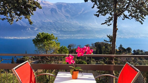 Een terras met een tafel en stoelen, met uitzicht op een prachtig uitzicht van een meer en bergen.